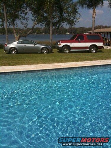 2007 Infiniti G35 coupe and a red and white Ford Bronco parked on grass by a pool