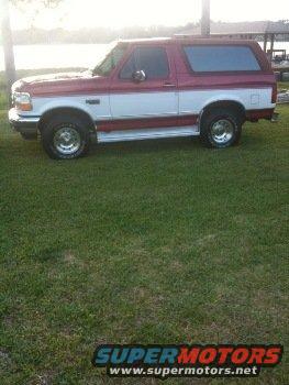 Two-tone red and white Ford Bronco parked on grass near water