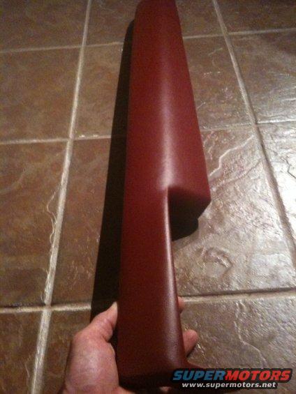 Red plastic interior trim piece held by a hand over a tiled floor