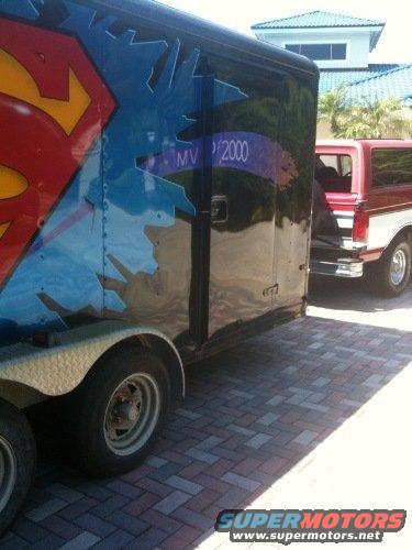 Trailer with Superman logo and a red and white SUV parked on brick pavers