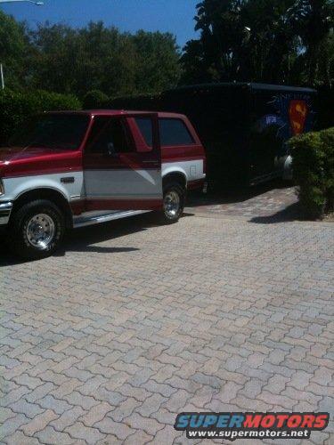 Red and white SUV with driver door open, parked next to a black trailer with Superman logo