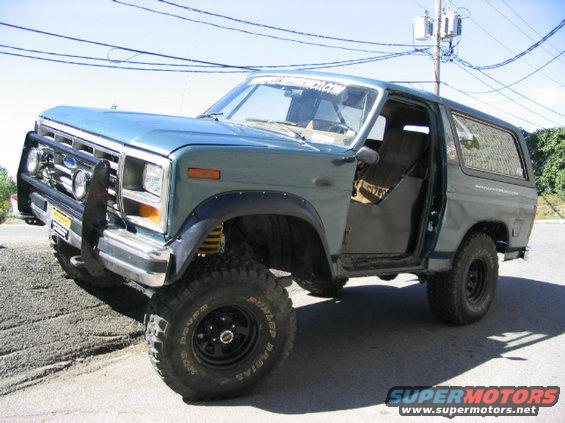 Blue Ford Bronco with aftermarket bumper and lifted suspension. Driver's door is open
