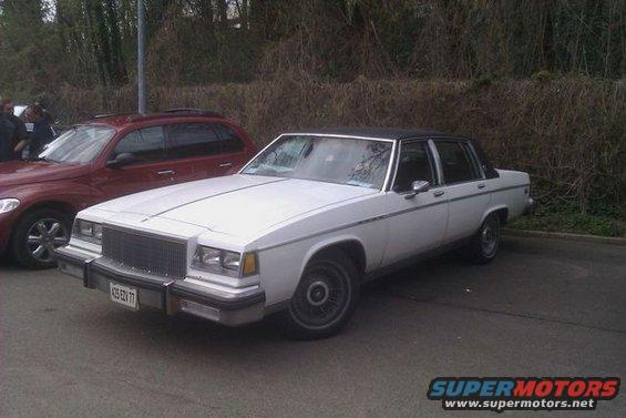 White sedan with black vinyl roof parked next to a red SUV. License plate reads 425 EDV 77