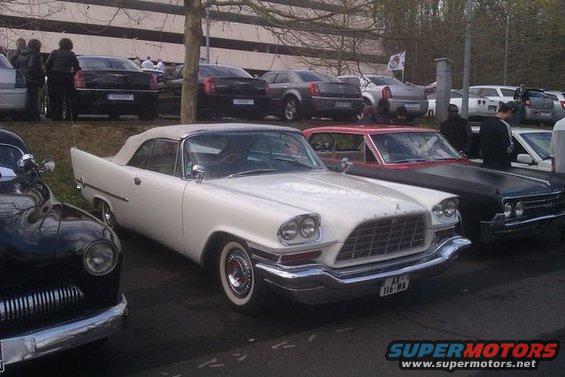 White convertible with fins and chrome grille parked next to a black car