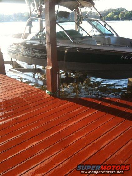 Boat on a lift next to a wooden dock. Another boat is visible behind it
