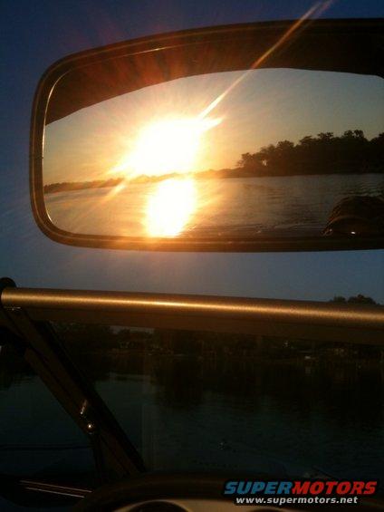 Sunset over water reflected in a boat's side mirror, with a golden bar across the foreground