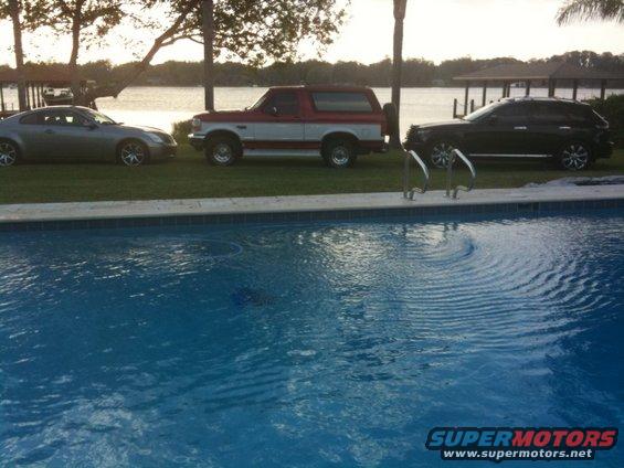 Silver coupe, red and white SUV, and black SUV parked by a pool