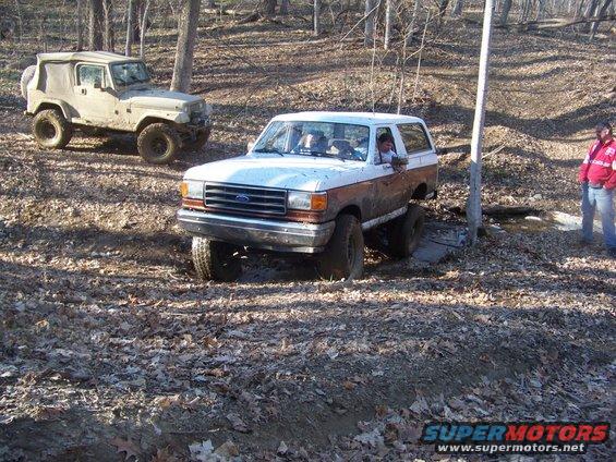 1989 Ford Bronco off-roading in woods with another Jeep