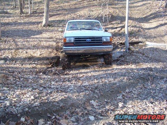 White Ford Bronco with a brown grille and bumper stuck in mud, front view