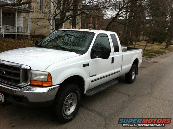 White Ford pickup truck parked on a street. It has a crew cab and a long bed