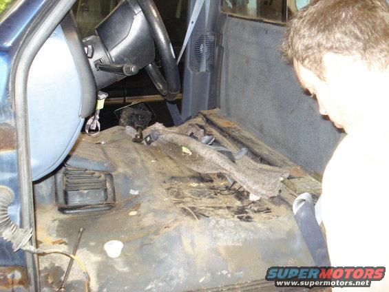 Interior of a truck cab, showing the floor and steering column. A person is looking into the cab