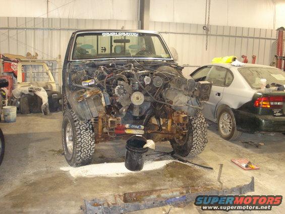 Truck with front end removed, showing engine and chassis. Off-road tires. "ROUGH COUNTRY" sticker on windshield