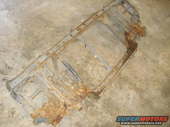 Rusted metal frame with rectangular cutouts and mounting holes, lying on a concrete floor