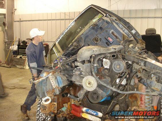 1993 Ford F-150 engine bay with extensive damage and a person inspecting it