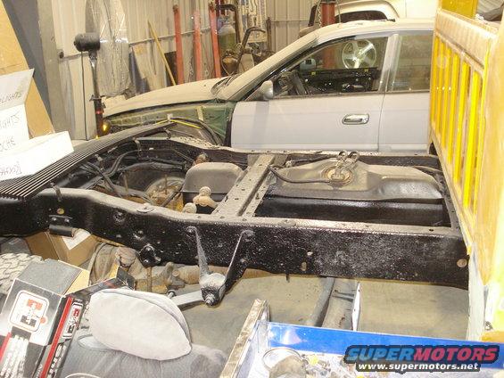 Truck chassis with fuel tank, next to a disassembled car
