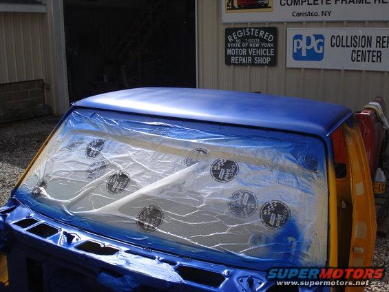 Blue truck cab with plastic sheeting over the windows, undergoing paint work. A "Supermotors.net" watermark is visible