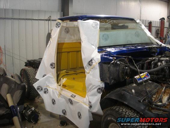Blue Ford F-150 truck cab with yellow interior, partially covered in protective sheeting, undergoing restoration