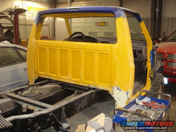 Yellow and blue truck cab and chassis undergoing restoration, showing the interior and frame