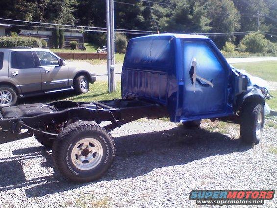 Blue pickup truck cab and chassis being painted, with another SUV parked nearby