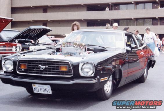Customized black Ford Mustang II with exposed engine and red side stripes. License plate reads 'NO PONY'
