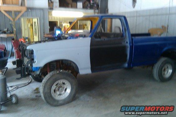 1993 Ford F-150 pickup truck in a garage, with primer on the front fender and door, blue paint on the rest of the cab and bed