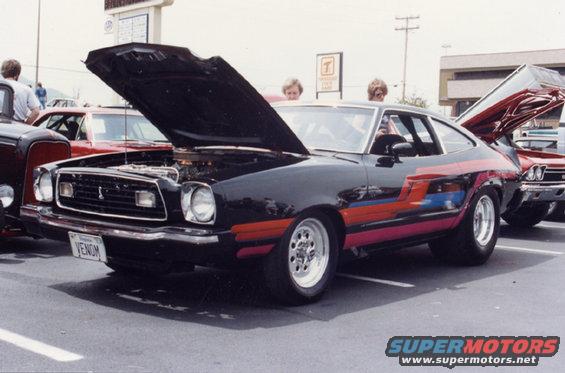 Black Ford Mustang II with colorful side stripes, hood open, parked next to other cars