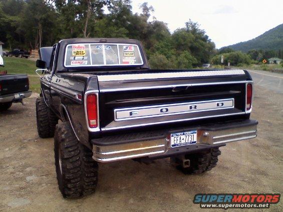Black lifted Ford pickup truck, rear view. Chrome bumper, "FORD" tailgate lettering, large off-road tires