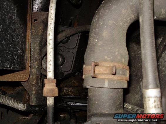 Engine bay hoses and metal brackets with rust. A white pipe is visible on the left