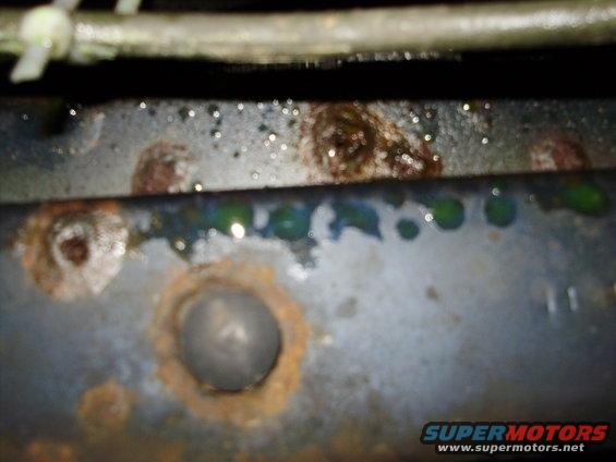 Rusted metal frame with green fluid drips and Supermotors.net watermark