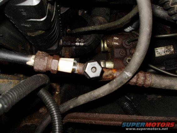 Close-up of a rusty metal fuel line fitting with a white plastic insert and a hexagonal nut