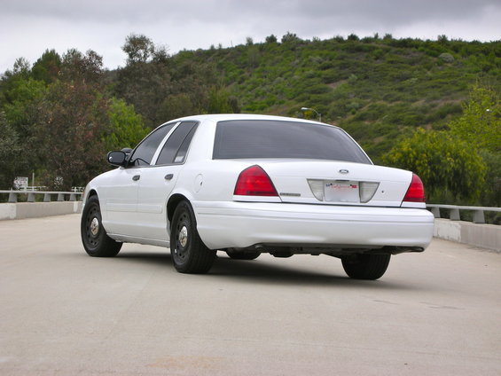 2004 Ford Crown Victoria sedan, rear 3/4 view, parked on a road with a grassy hill in background