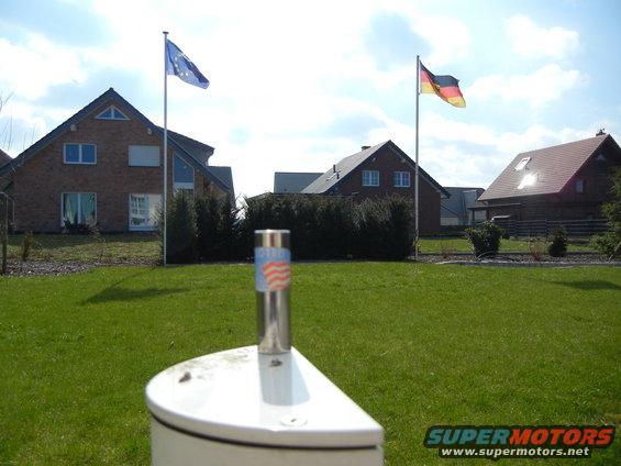 Metal object with American flag pattern on a white base, with houses and flags in the background