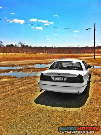 White 2000 Ford Crown Victoria parked on gravel with puddles, rear view