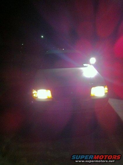 Car headlights on at night. Supermotors.net logo visible