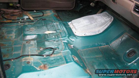 Interior floor of a vehicle with seats removed, showing rust and exposed wiring