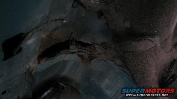 Rusted hole in vehicle floor pan with torn carpet