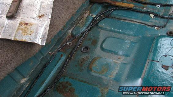 close-up of rusty teal floor pan with wiring harness