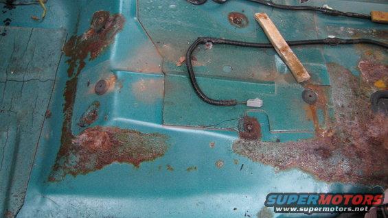 Rusted teal interior floor pan with wiring harnesses visible