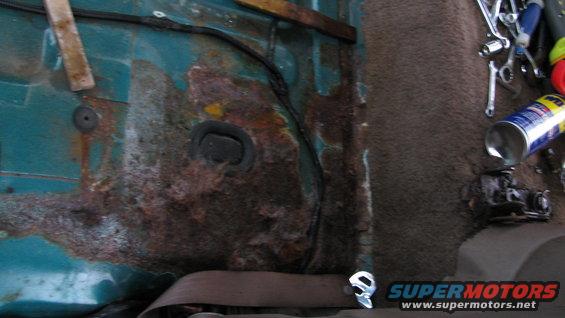 Teal interior panel with significant rust damage, showing a seatbelt buckle and tools