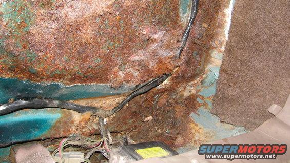 rusted interior floor pan with exposed wiring and a yellow label box
