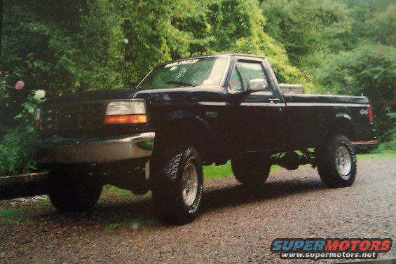 Black Ford F-150 pickup truck, lifted, with chrome bumper and aftermarket wheels, parked on a gravel surface