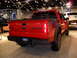 2011 Ford F-150 - A red Ford F-150 Raptor pickup truck is displayed indoors, with another vehicle visible in the background.