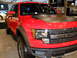 2011 Ford F-150 - A red Ford F-150 Raptor truck is displayed indoors, with 'LINCOLN' visible in the background.