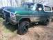 1979 Ford Bronco - A muddy green Ford Bronco with a white top is parked off-road on a dirt path.