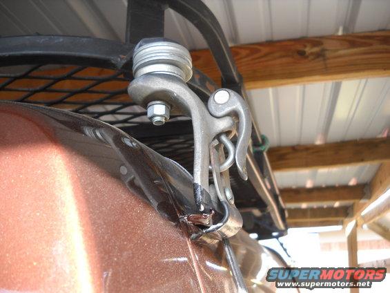 Close-up of a metal clamp attached to a brown vehicle's roof edge, with a black roof rack above