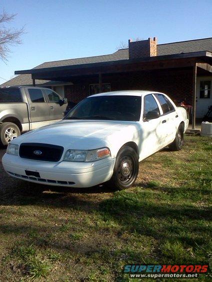 White 2007 Ford Crown Victoria parked in front of a house with a pickup truck next to it