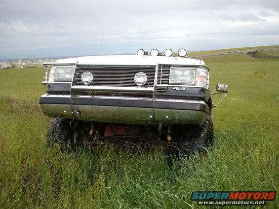 White Ford Bronco with chrome grille guard and four roof lights, front view, in tall grass