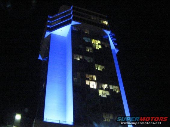 Tall building at night with blue lights illuminating part of its facade. Windows are lit