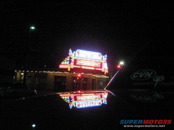 Dark car hood reflecting a brightly lit neon sign of a building at night