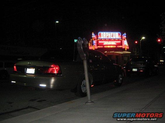 Gold Mercury Grand Marquis parked at night, rear view. Orpheum theater sign in background